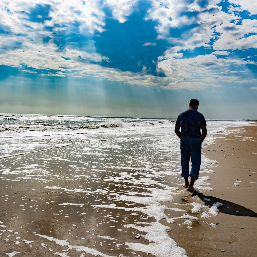 man walking on the shore on a cloudy day