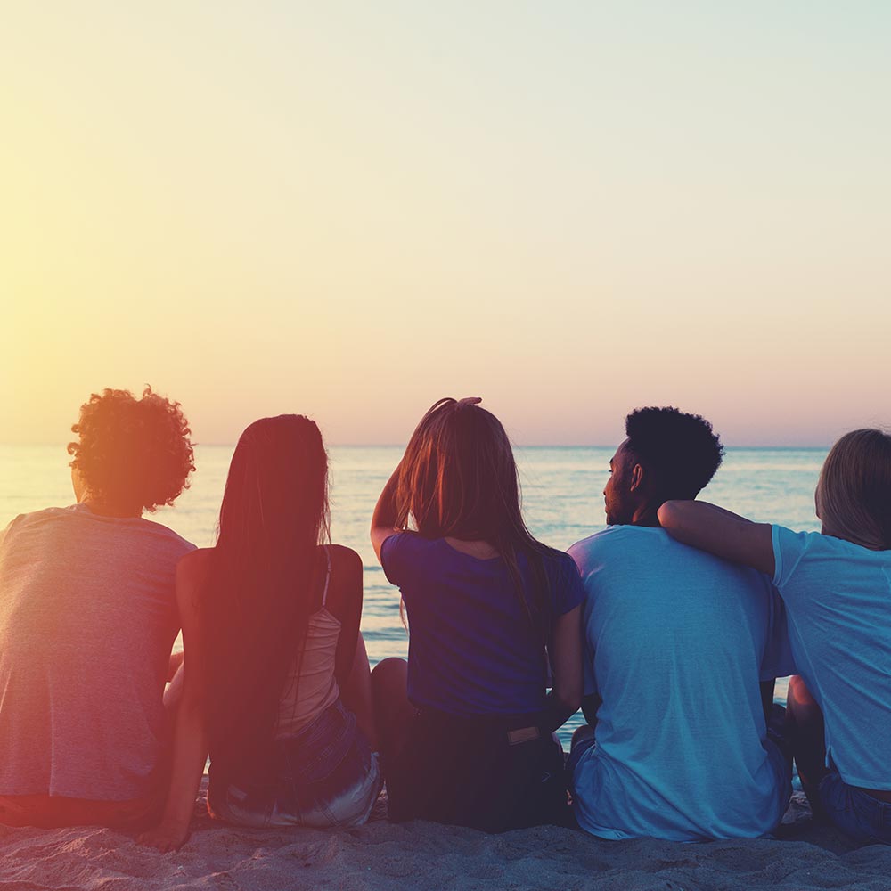 Group of happy friends relaxing at the beach during sunset