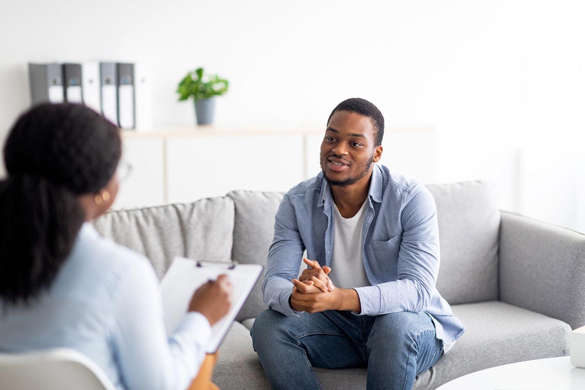 Young black guy talking to psychologist receiving professional help at mental health clinic