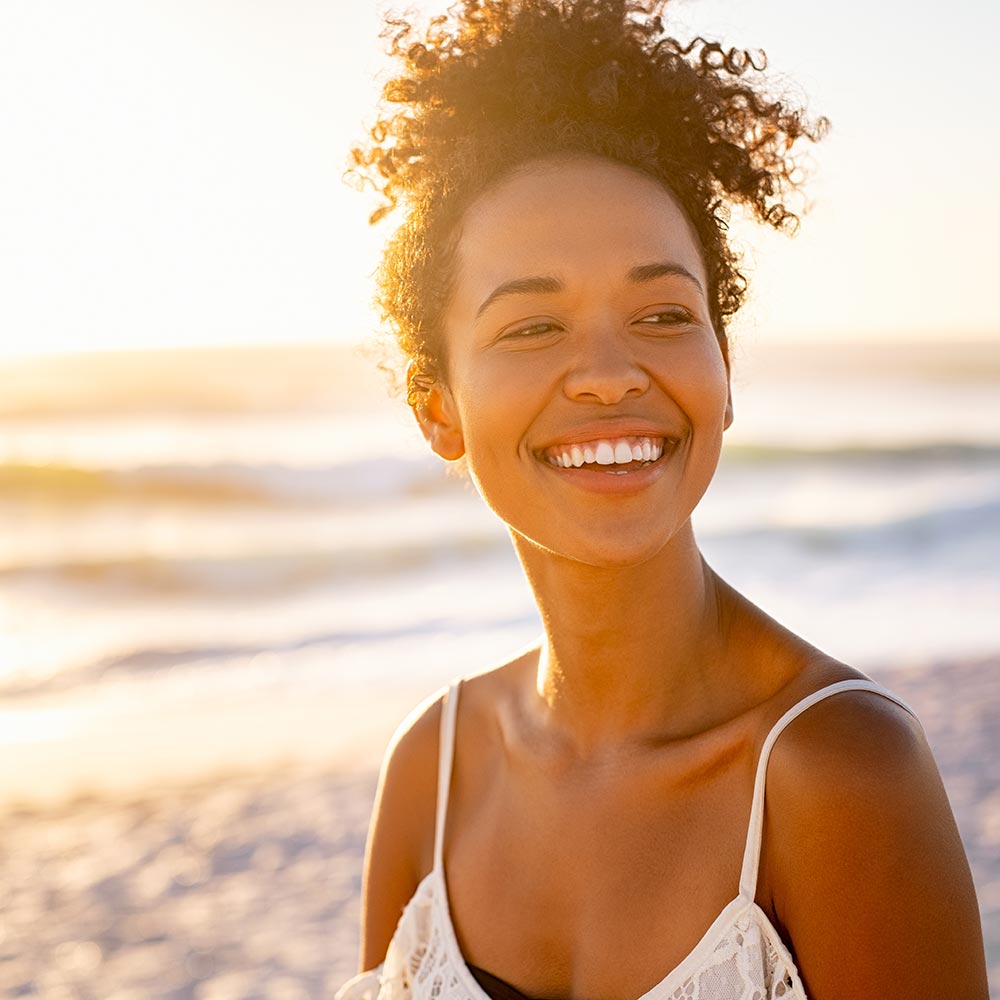 Smiling young black woman in beachwear enjoy sunset at beach
