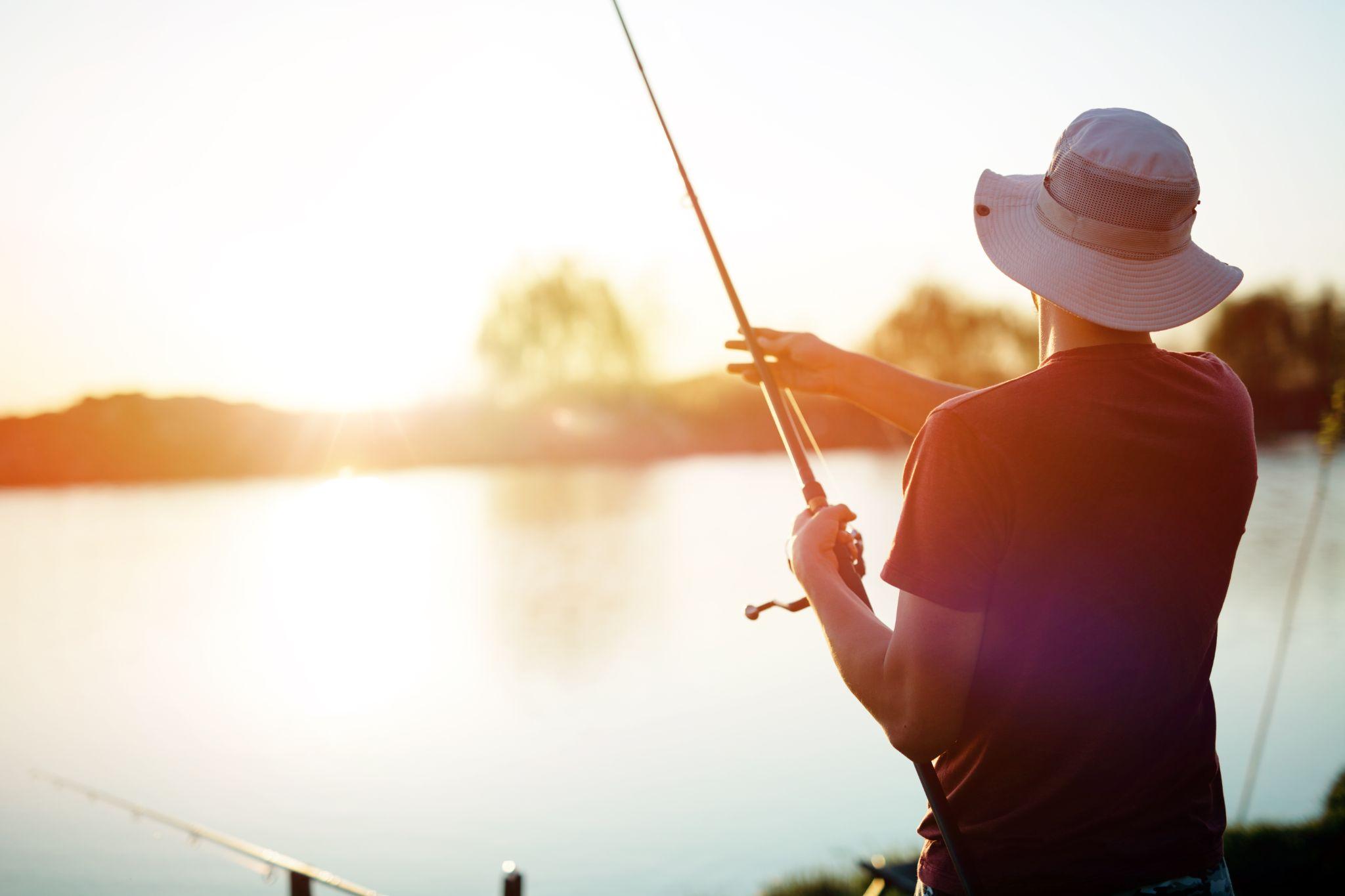 Young man fishing on a lake at sunset and enjoying hobby