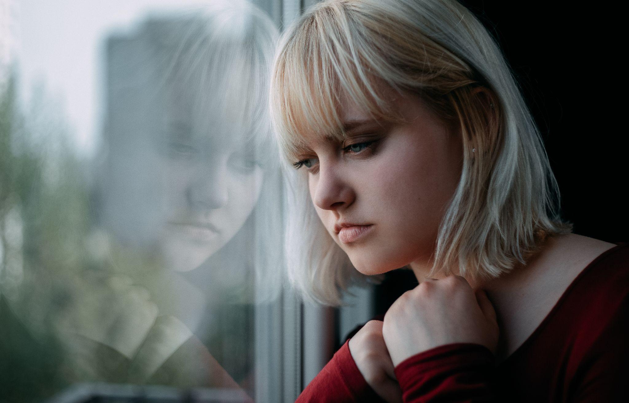 Portrait of depressed young blond woman near window at home