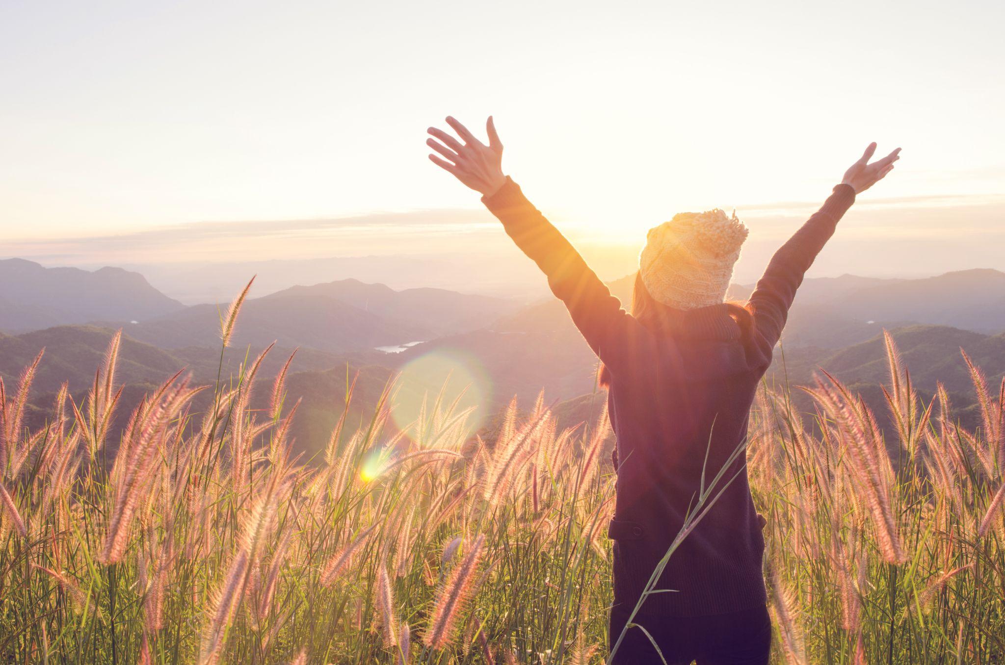 Carefree Happy Woman Enjoying Nature on grass meadow on top of mountain cliff with sunrise.