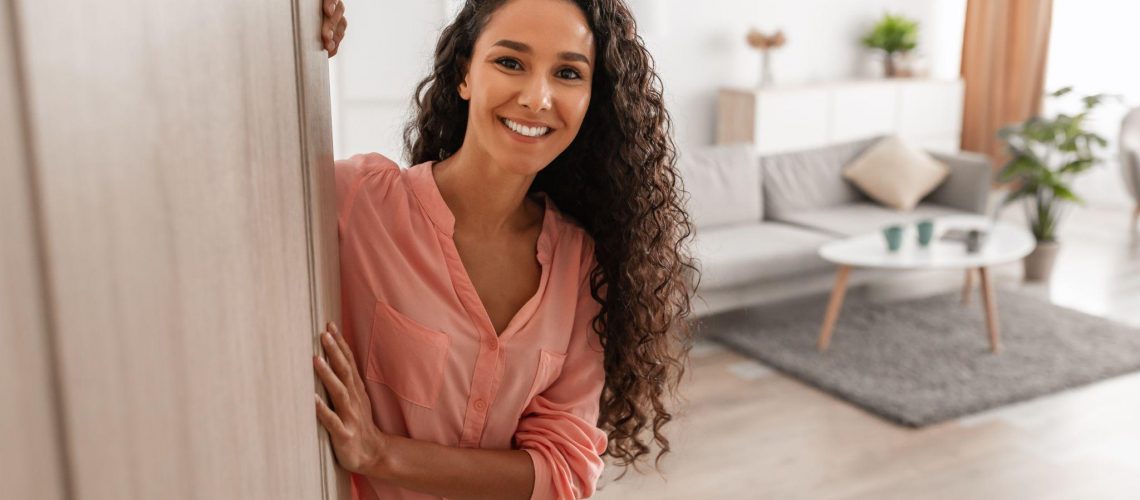 Cheerful young curly lady inviting people to enter home