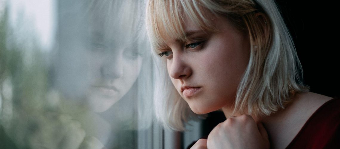Portrait of depressed young blond woman near window at home